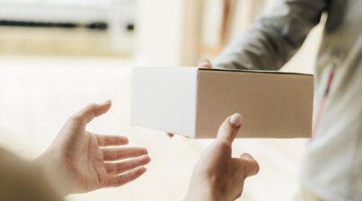 A mão de uma pessoa entregando uma caixa de papelão para outra mão.